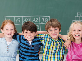 Schulanfang und Einschulung - 6 Kinder stehen lachend und Arm in Arm vor einer beschriebenen Schultafel