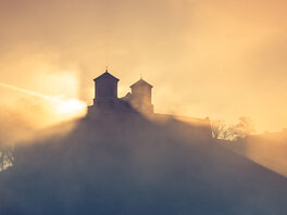 Im Nebel scheint Sonne in der Dämmerung im hinter zwei Klostertürmen durch.