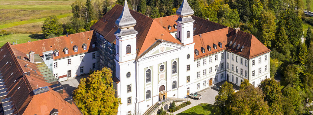 Luftbild vom Kloster Schlehdorf mit zwei Türmen und kleinem Wald.