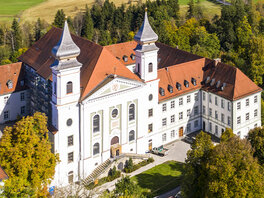 Luftbild vom Kloster Schlehdorf mit zwei Türmen und kleinem Wald.