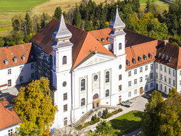 Luftbild vom Kloster Schlehdorf mit zwei Türmen und kleinem Wald.