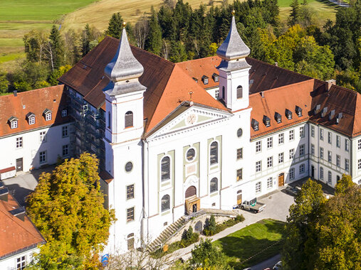 Luftbild vom Kloster Schlehdorf mit zwei Türmen und kleinem Wald.