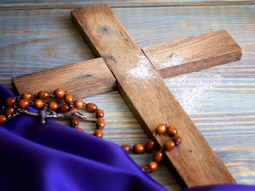 Schlichtes Holzkreuz, Rosenkranz, violettes Tuch, halber Brotlaib und Wasser, Bargeld (5€-Scheine, 1€-Münze),