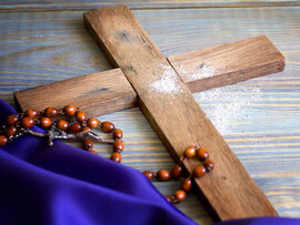 Schlichtes Holzkreuz, Rosenkranz, violettes Tuch, halber Brotlaib und Wasser, Bargeld (5€-Scheine, 1€-Münze),