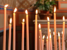 Eine Reihe langer dünner brennender Kerzen vor einem Altar.