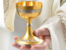 Goldener Kelch in der linken Hand eines Priesters.
