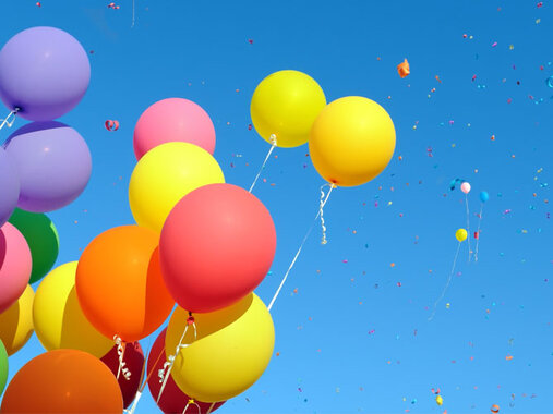 Ein Bündel schwebende bunte Luftballons vor blauem Himmel.