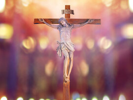 Figur Jesu am Kreuz mit Aufschrift INRI vor unscharfem Lichtermeer.
