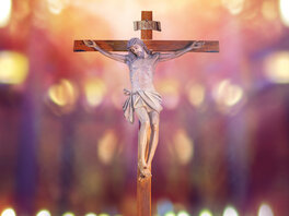 Figur Jesu am Kreuz mit Aufschrift INRI vor unscharfem Lichtermeer.