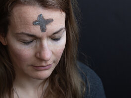 Frau mit Aschekreuz auf der Stirn und andächtig geschlossenen Augen.