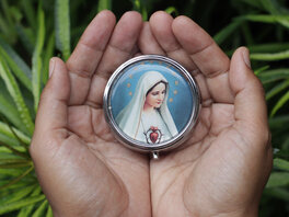 Medallion in den Händen einer Person, mit Darstellung Marias mit Herz, weißem Schleier und Sternenkranz