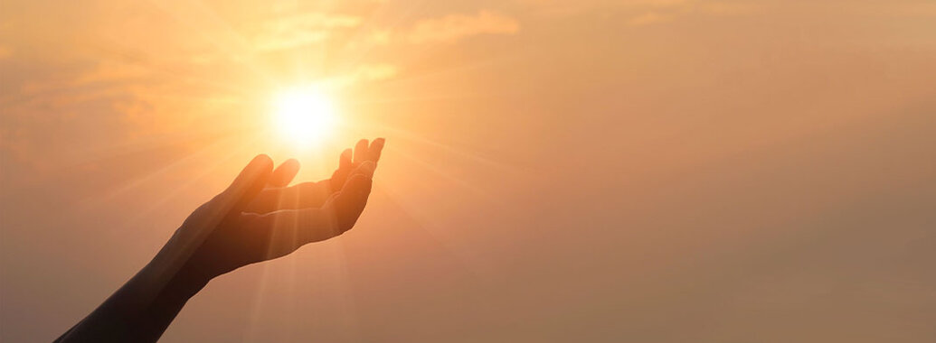 Foto auf dem die Silhouette einer nach oben geöffnete Handfläche, die Sonne am Himmel umfasst.
