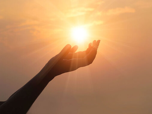 Foto auf dem die Silhouette einer nach oben geöffnete Handfläche, die Sonne am Himmel umfasst.