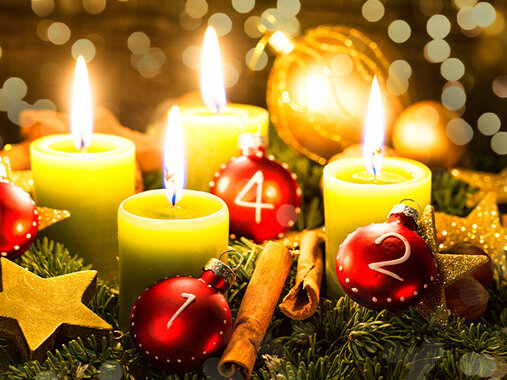Advent - Adventskranz aus Tannengrün, mit vier kräftig leuchtenden entzündeten Kerzen, Zimtstangen, Sternen und roten, sowie goldenen Kugeln. Vor Gold funkelndem Hintergrund.
