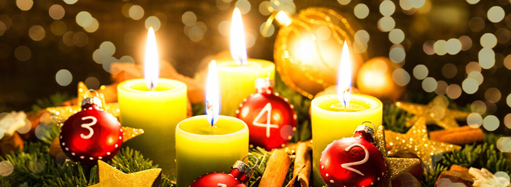 Advent - Adventskranz aus Tannengrün, mit vier kräftig leuchtenden entzündeten Kerzen, Zimtstangen, Sternen und roten, sowie goldenen Kugeln. Vor Gold funkelndem Hintergrund.