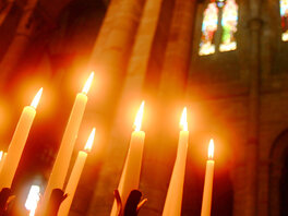 orange leuchtende, brennende Kerzen in dunkler Kirche