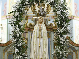 Madonna mit einem Rosenkranz über gefalteten Händen, Krone und weißem Gewand, umgeben von einem Blumenkranz mit weißen Blüten.