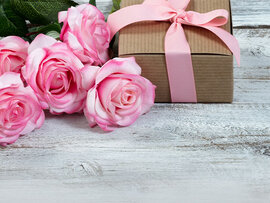 Sechs blühende rosa Rosen und ein Geschenkschachtel mit rosa Schleife.