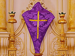 Mit einem violetten Fastentuch überhangenes Kreuz, vor einem in Goldtönen gehaltem Hochaltar. Das Tuch ist mit florale Ornamenten und einem Goldenem Kreuz verzirrt.
