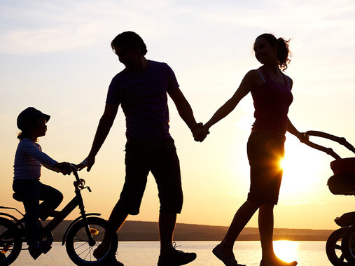Lebenskreis - Die Silhouette einer Familie, Vater, Mutter, ein kleiner Junge auf einem Fahrrad und ein Kinderwagen im Gegenlicht eines Sonnenunterganges.