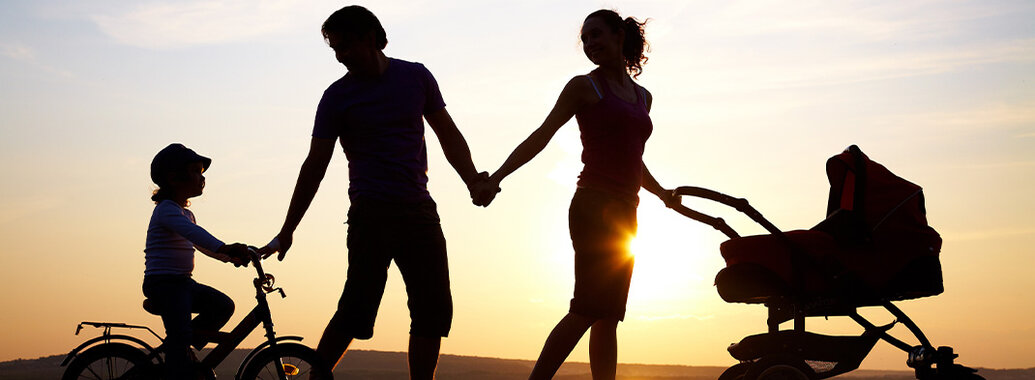 Lebenskreis - Die Silhouette einer Familie, Vater, Mutter, ein kleiner Junge auf einem Fahrrad und ein Kinderwagen im Gegenlicht eines Sonnenunterganges.