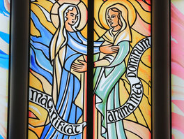 Schwangere Maria umarmt Elisabet. Text: magnificat anima mea dominum.