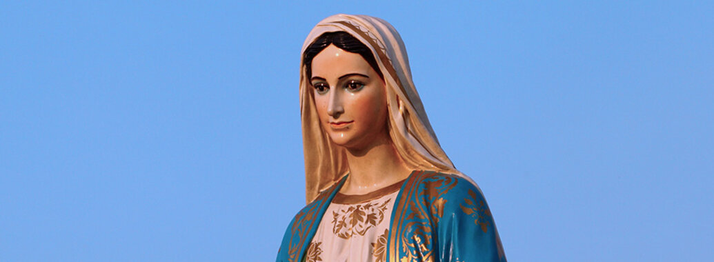 Marienfeste - Oberkörper einer Madonna mit Schleier, in einem rosa und blauen Gewand mit auffälligen Goldverzierungen vor klarem blauen Himmel.