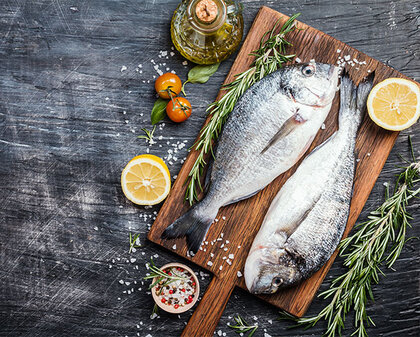 Zwei ungekochte Fische hübsch arrangiert auf einem Holzbrett