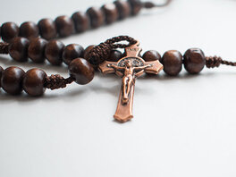 Rosenkranz aus dunklen Holzperlen mit bronzenem Kreuz mit Jesus und der Inschrift "INRI".
