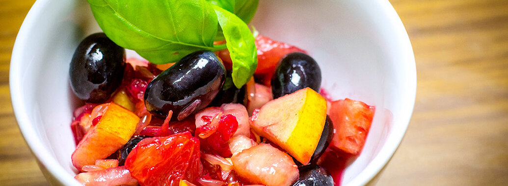 Schälchen bunter Obstsalat mit dunklen Trauben, saftiger Blutorange. Garniert mit frischen Basilikumblättern.