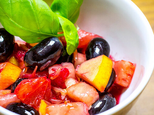 Schälchen bunter Obstsalat mit dunklen Trauben, saftiger Blutorange. Garniert mit frischen Basilikumblättern.