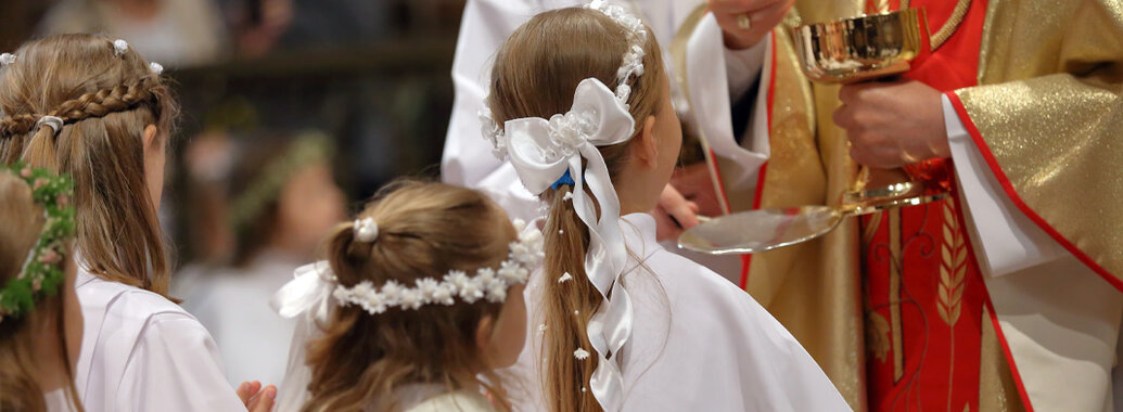 Mädchen mit weißer Haarschleife und Kommunikationskleid beim empfangen der ersten Kommunion.