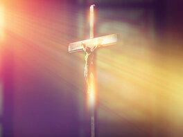  Kreuz mit Jesus im Lichtbündel eines durchschienenen bunten Glasfensters.