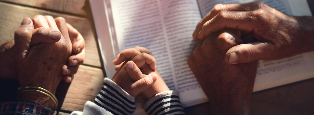 Kirchenjahr - Gefaltete Hände dreier Menschen unterschiedlichen Lebensalters über einem Gebetsbuch. In der Mitte die Hände eines Kindes.