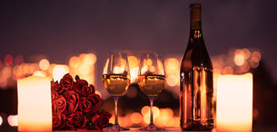 Romantisches Candle Light Dinner mit zwei Gläsern Wein, Rosen, einer Weinflasche und Teelichtern