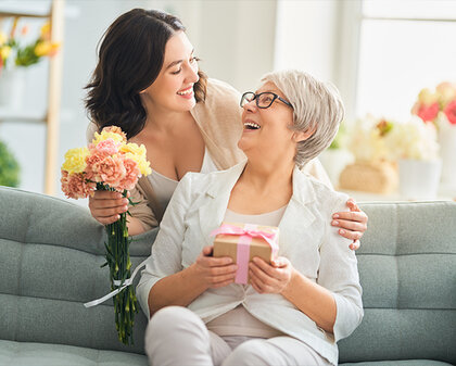 Tochter mit Blumen und Mutter mit verpacktem Geschenk