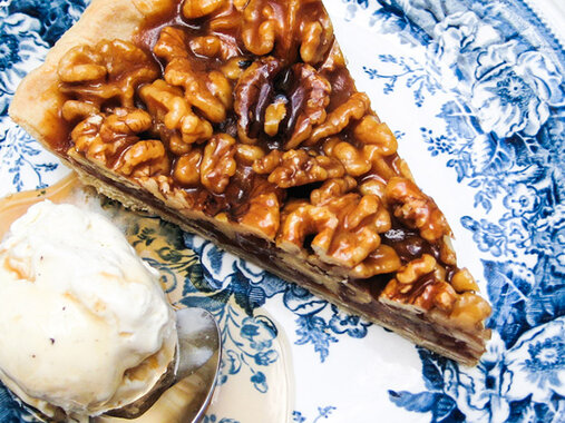 Stück Walnusstarte bedecktmit glänzender Wallnuss-Karamell-Schicht, dazu ein Kugel cremiges Vanilleeis mit zerfließend-goldigem Ahornsirup.