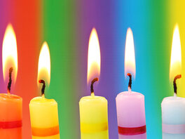 Geburtstag - eine Reihe buntgemusterter, brennender Kerzen vor buntem Hintergrund