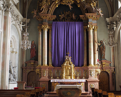 Hochaltar, dessen Mittelteil mit einem violetten Tuch geschmückt ist
