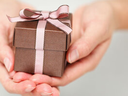 Kleine bronzene Geschenkschachtel mit rosa Schleife in reichenden Händen.