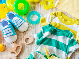 Getreifte Babykleidung, Schuhe, Mütze, Zahnbürste, Kamm und diverses Spielzeug, darunter Quietscheente, kleines Holzpferd, Ringe.