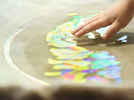 Kinderhand fast in Becken mit bunt schimmerndem Wasser,