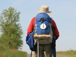 Pilgerer auf Weg mit Wanderaustattung. Rucksack mit Jakobsmuschel, Hut, Wanderstock, Regenjacke.
