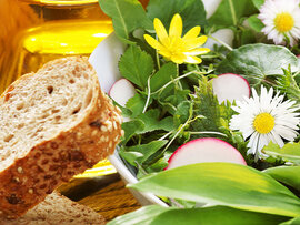 Frischer Salat aus grünen Kräutern und essbaren Blumen mit Radieschen, dazu Brotstücke.