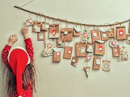 Mädchen greift nach selbst gebasteltem Adventskalender an der Wand über ihm