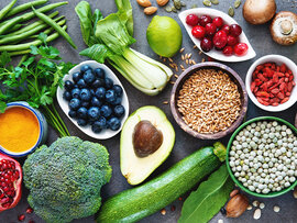 Auswahl an Lebensmitteln: Linsen, Bohnen, Aubergine, Rosenkohl, Granatapfel, grüne Bohnen, Brokkoli, Petersilie, Heidelbeeren, Pak Choi, Avocado, Zitrone, Getreide, Zucchini, Cranberries, Mandeln, Ingwer, Gojibeeren, Champignons, Chiasamen, Apfel, Kürbiskerne