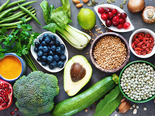 Auswahl an Lebensmitteln: Linsen, Bohnen, Aubergine, Rosenkohl, Granatapfel, grüne Bohnen, Brokkoli, Petersilie, Heidelbeeren, Pak Choi, Avocado, Zitrone, Getreide, Zucchini, Cranberries, Mandeln, Ingwer, Gojibeeren, Champignons, Chiasamen, Apfel, Kürbiskerne