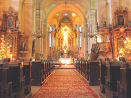 Kirchengang mit Teppich hinführend zu weihnachtlich dekorierten und festlich beleuchtetem Altar 