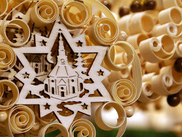 Adventsdekoration aus unterschiedlichen hellen zusammengesetzten Holzelementen. Das Zentrum bildet eine sternförmige Laubsägearbeit, die eine Kirche darstellt. 