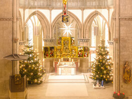 Hell erleuchteter Altarraum mit hängendem Weihnachtsstern, eingerahmt von zwei prächtigen Weihnachtsbäumen.